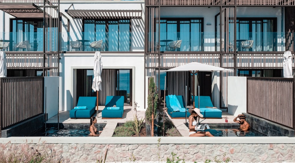 Luxe swim-up kamers met gasten die ontspannen in het zwembad, inclusief priv&eacute;terras met dikke blauwe ligbedden in de zon.